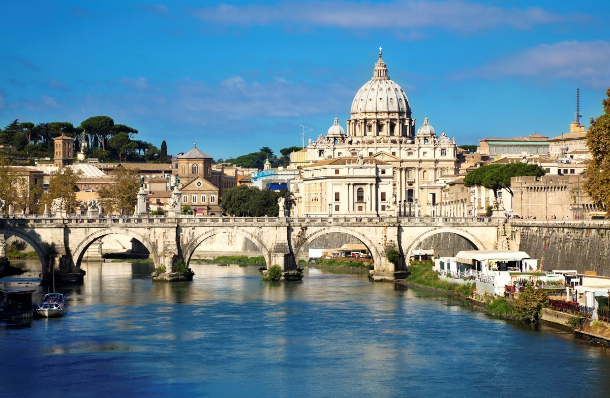 Bridge over river with St. Peter's Basilica in the background under blue sky.