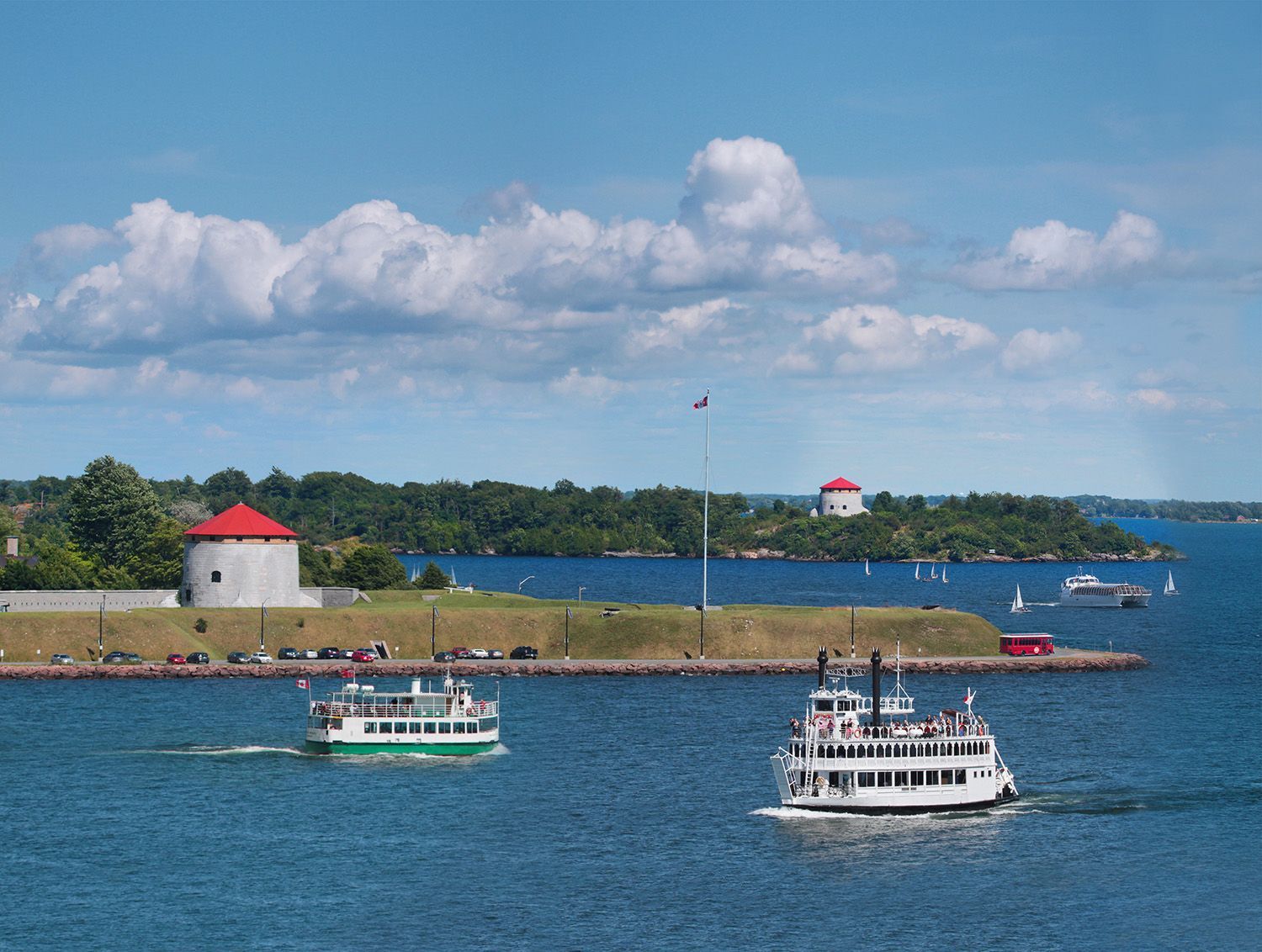 Two boats on a blue lake, with green trees and red-roofed towers on an island under a blue sky.
