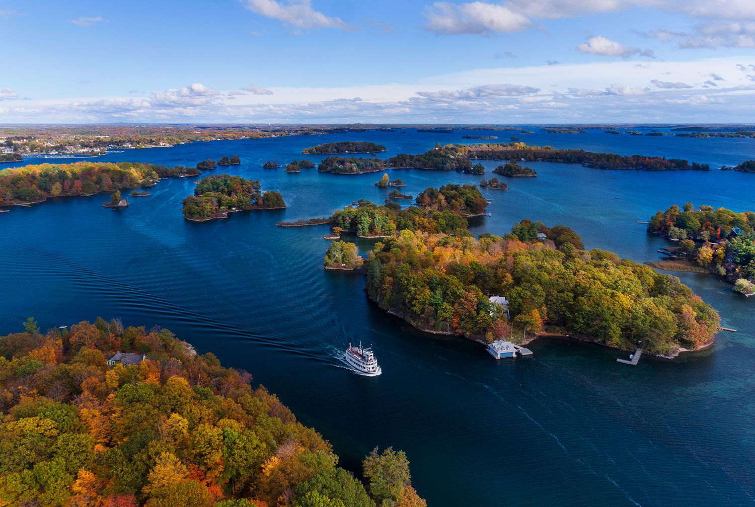 Aerial view of 1000 islands in a blue lake, with a boat traveling. Autumn foliage in vibrant colors.