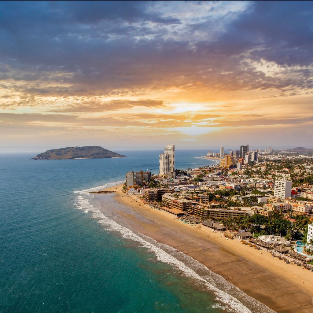 Aerial view of a coastal city skyline beside a long sandy beach at sunset