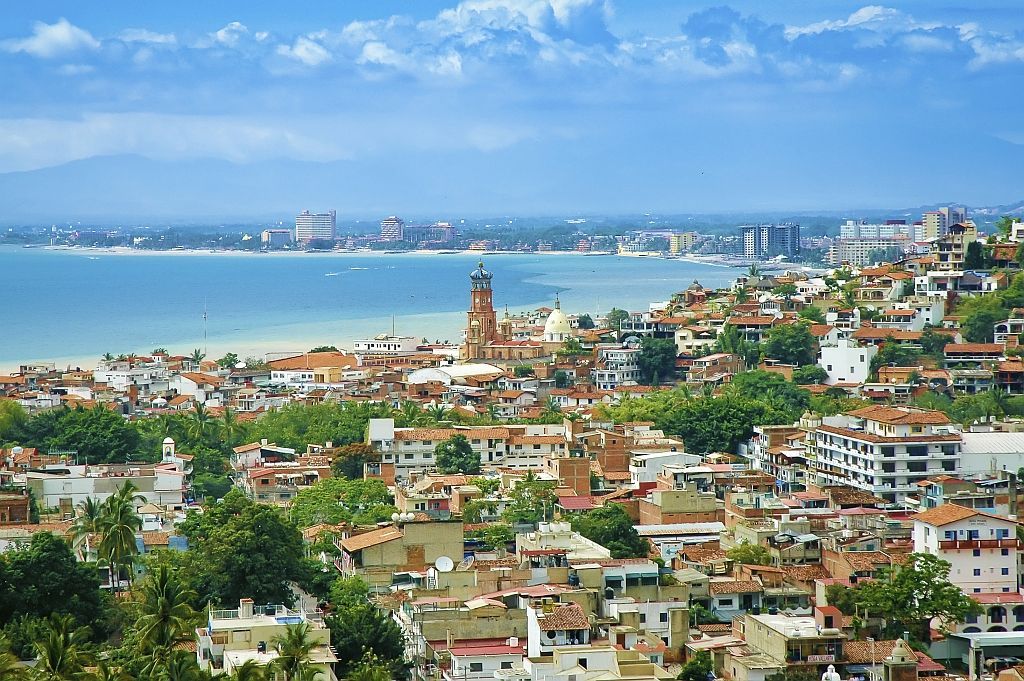 Coastal cityscape with colorful buildings, green hills, and a blue bay under a clear sky