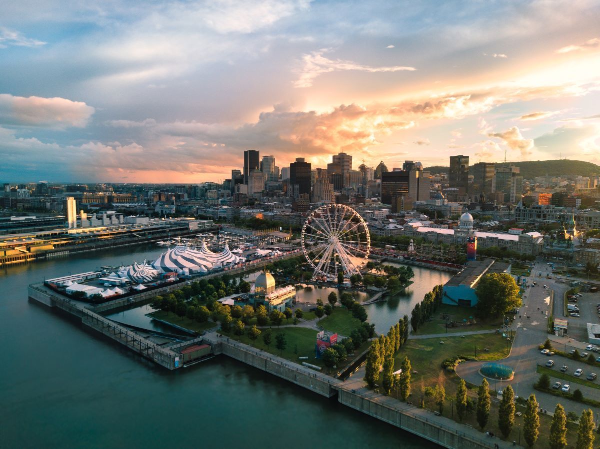 Aerial view of Montreal skyline, including a Ferris wheel, with water in foreground and sunset sky.