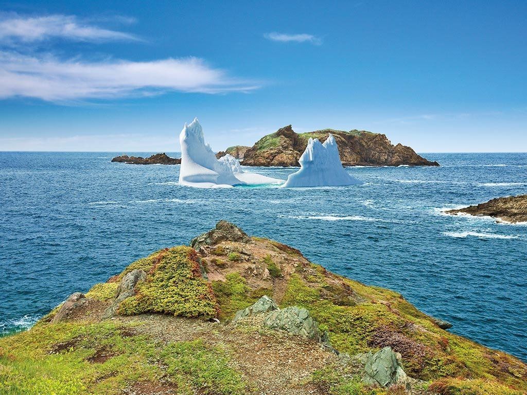 Ocean view with iceberg and rocky islands under a blue sky.