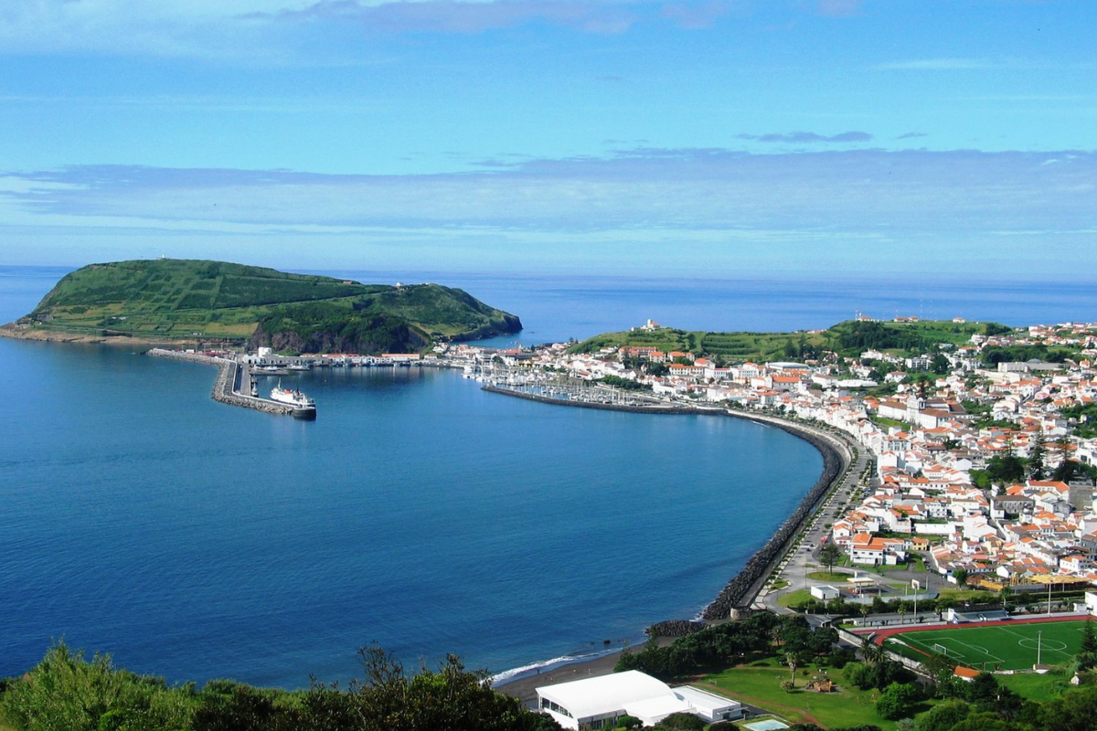 Coastal town and harbor with a small island in the background under a blue sky.