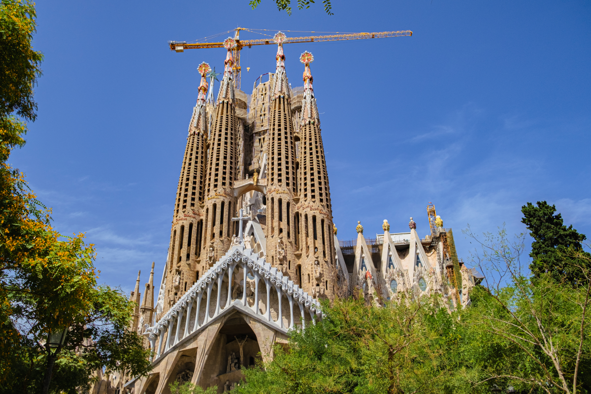 Sagrada Familia basilica under construction with blue sky, cranes, and trees.