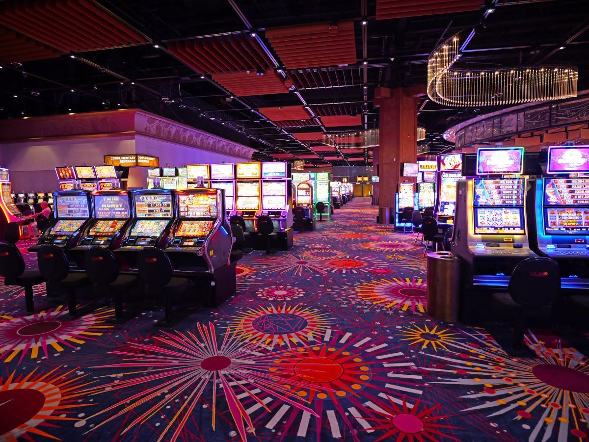 Casino interior with rows of slot machines on a patterned carpet under a dark ceiling.