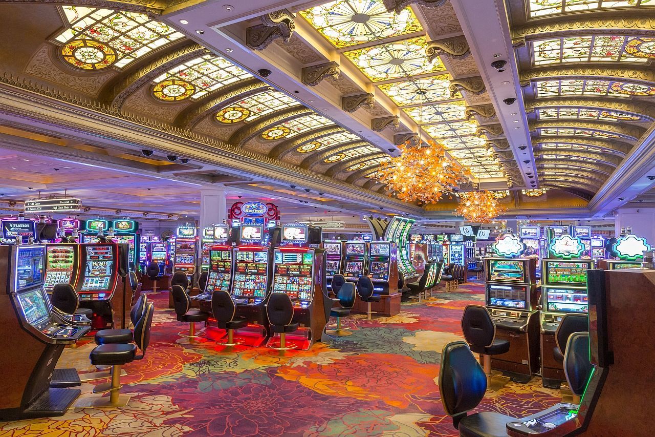 Casino interior with rows of slot machines and ornate stained-glass ceiling.