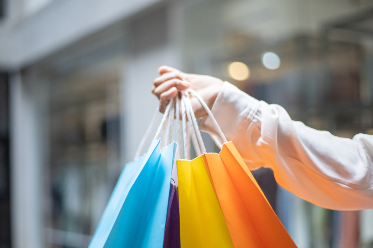 Hand holding colorful shopping bags in front of a store window.