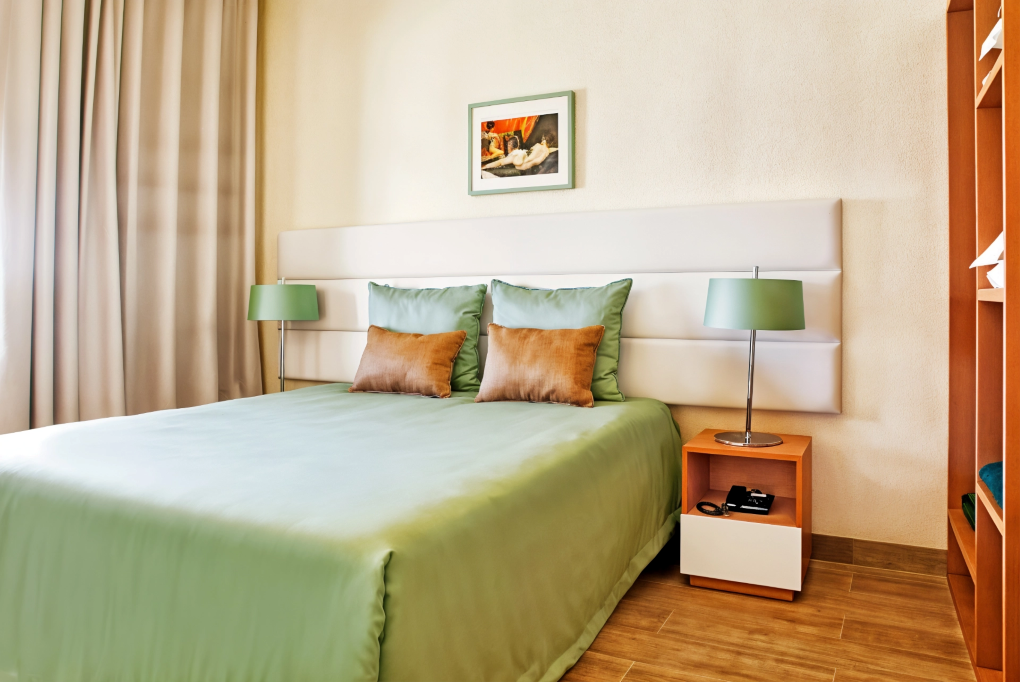 Small bedroom with a green bedspread, matching lamps, and a framed picture on the wall.