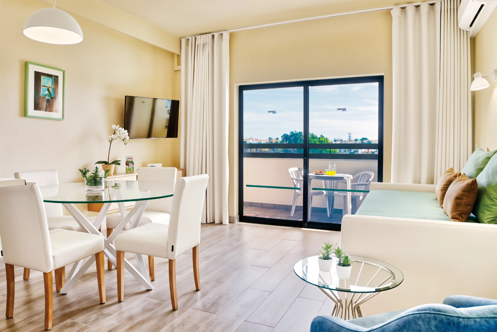 Bright modern living-dining room with balcony view, white furniture, and blue sofa accents