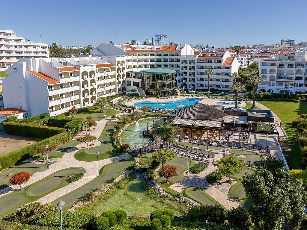 Resort hotel complex with pools, gardens, and white apartment buildings under a blue sky