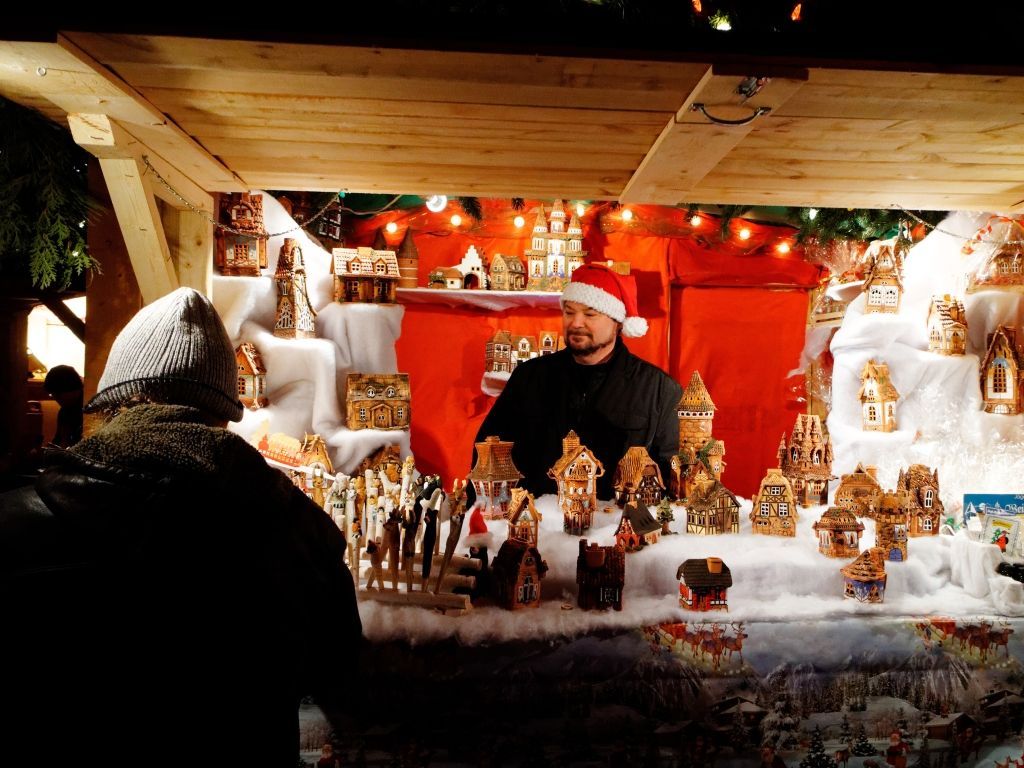 Festive holiday market stall with a vendor in a Santa hat and rows of handmade ornaments and decorations