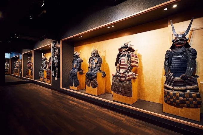A row of traditional Japanese samurai armor displayed in lit wall niches within a dimly lit museum gallery.