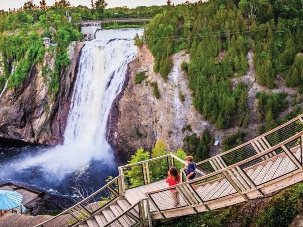 Montmorency Falls in Quebec. People on wooden stairs overlooking a large waterfall cascading into a dark pool.