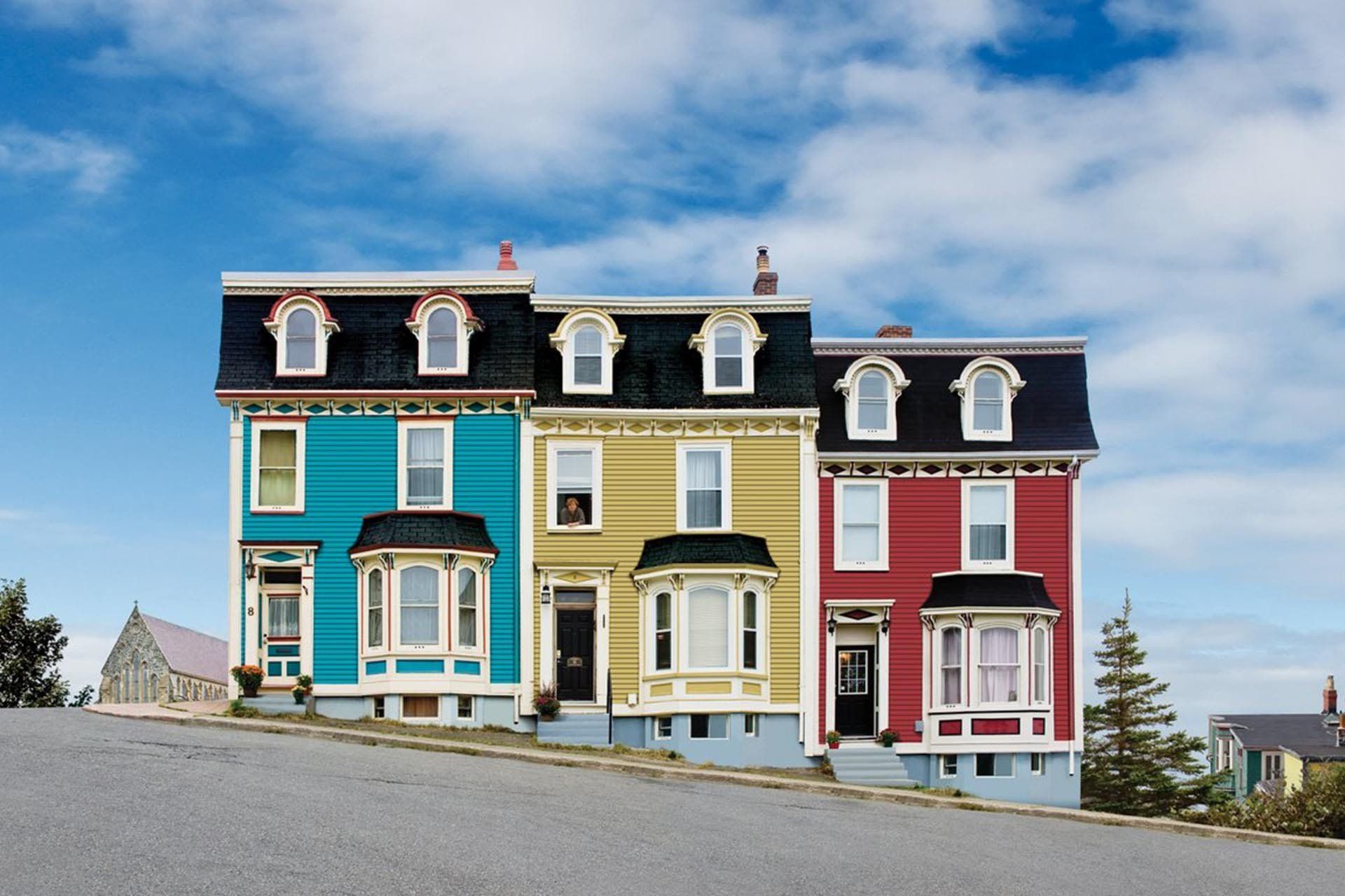 Three colorful Victorian houses on a sloped street under a blue sky.