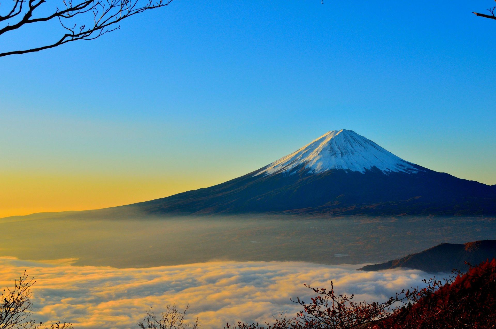 Mount Fuji, snow-capped, rises above a sea of clouds under a clear blue sky.