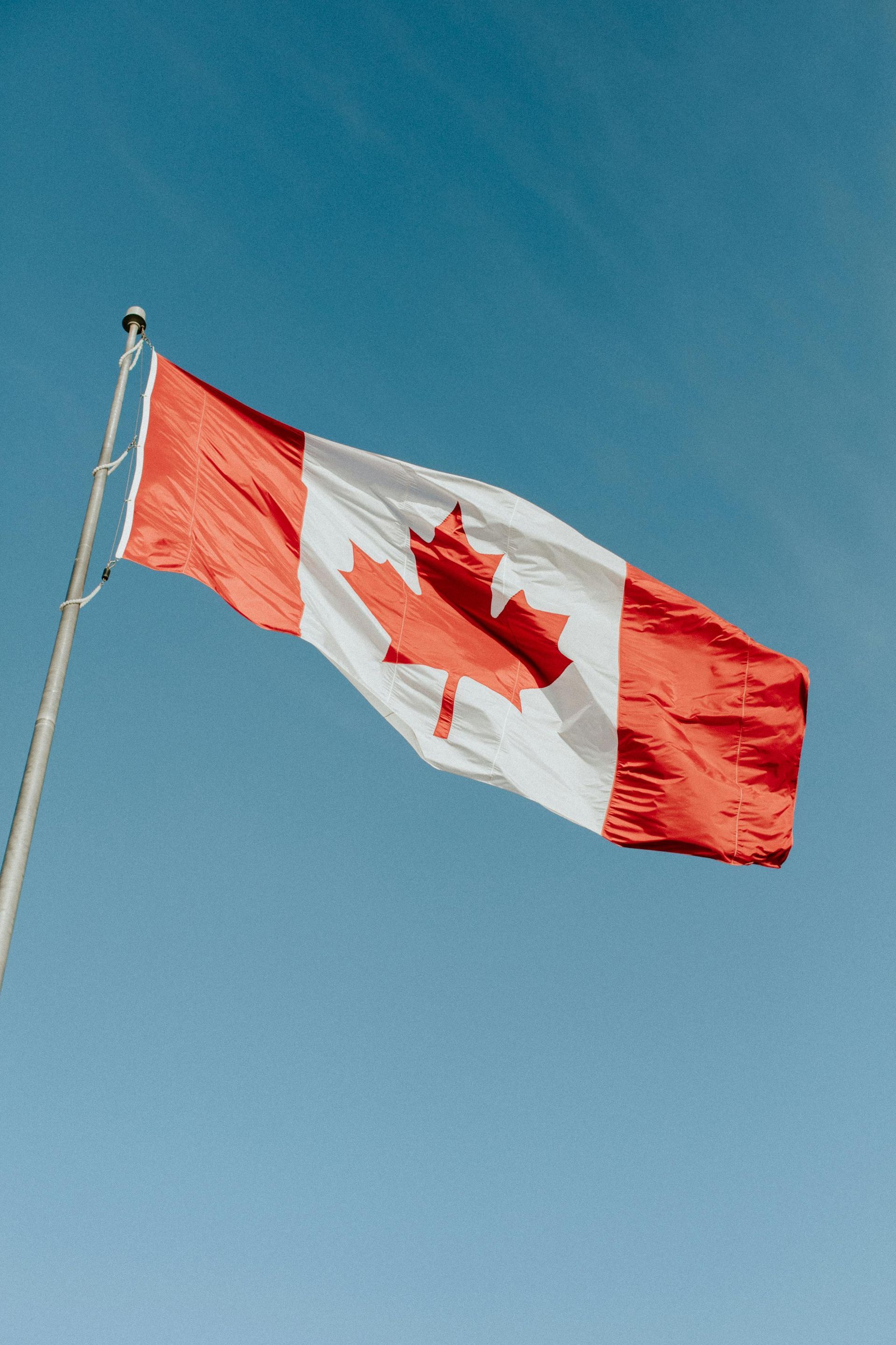 Woman with Canadian flag stands by turquoise lake, mountains in background.