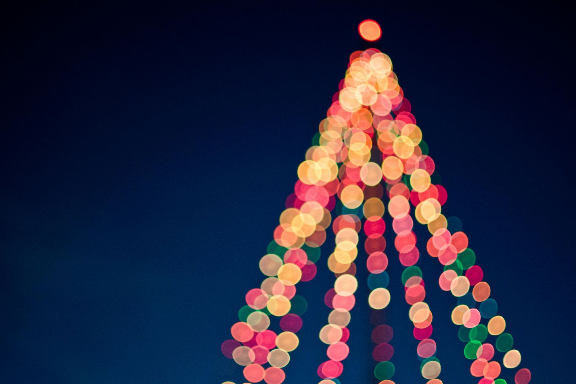 Blurred Christmas tree lights against a dark blue sky, with red, yellow, and green bokeh.