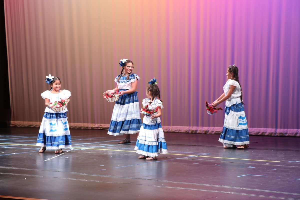 a group of young girls in blue and white dresses are dancing on a stage