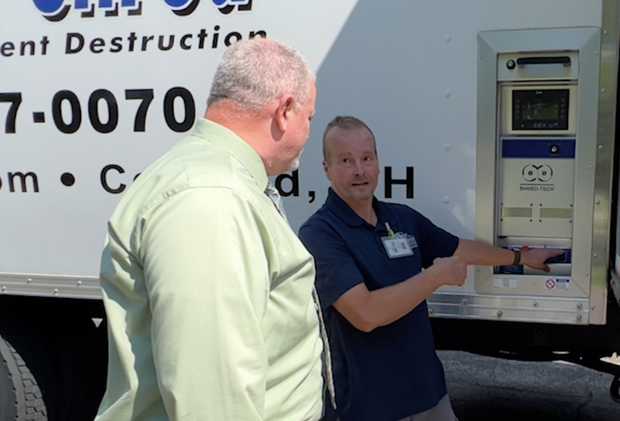 Two men stand beside a truck. One points to a panel, the other observes. White truck with blue details.
