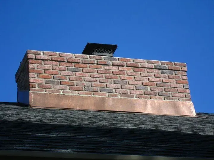 A brick chimney on top of a roof with a blue sky in the background