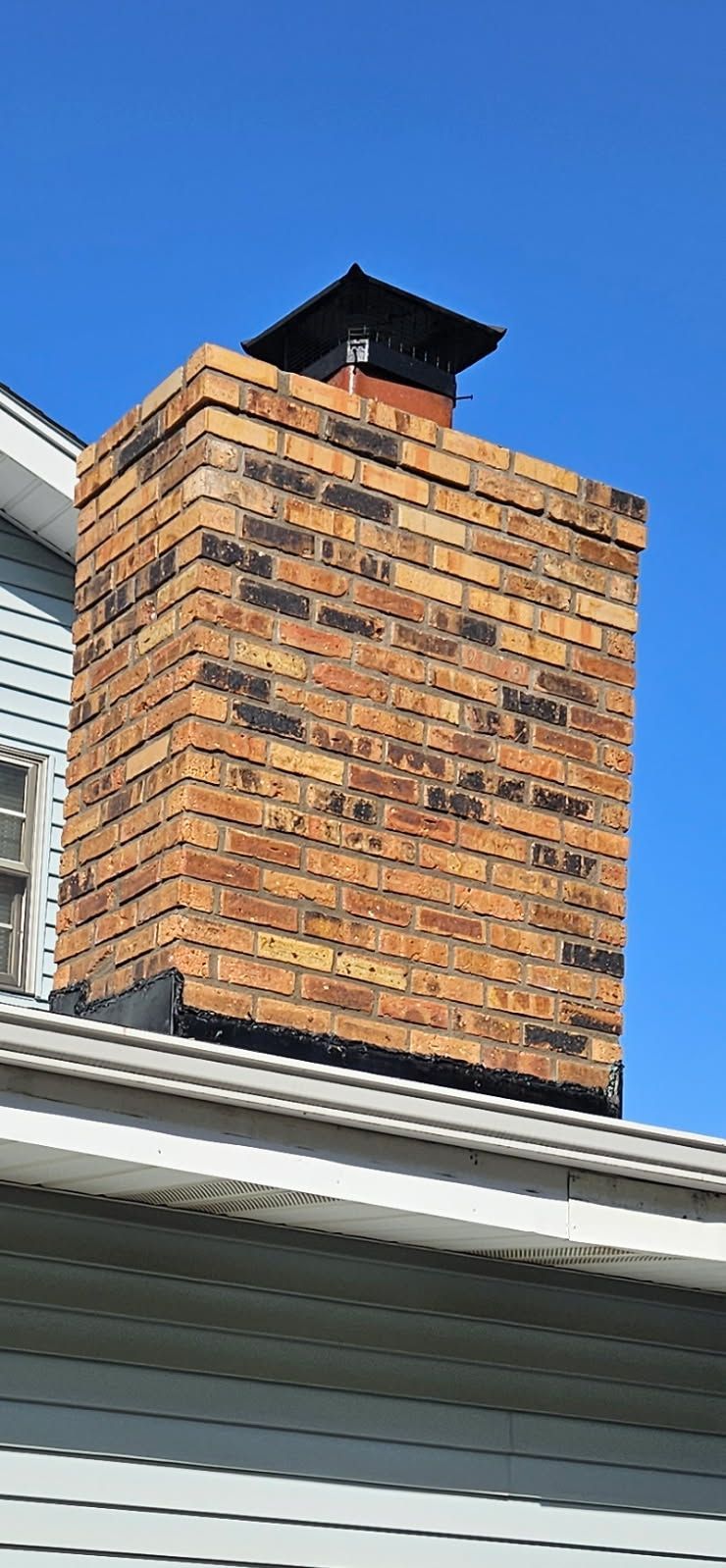A brick chimney on top of a roof next to a window.