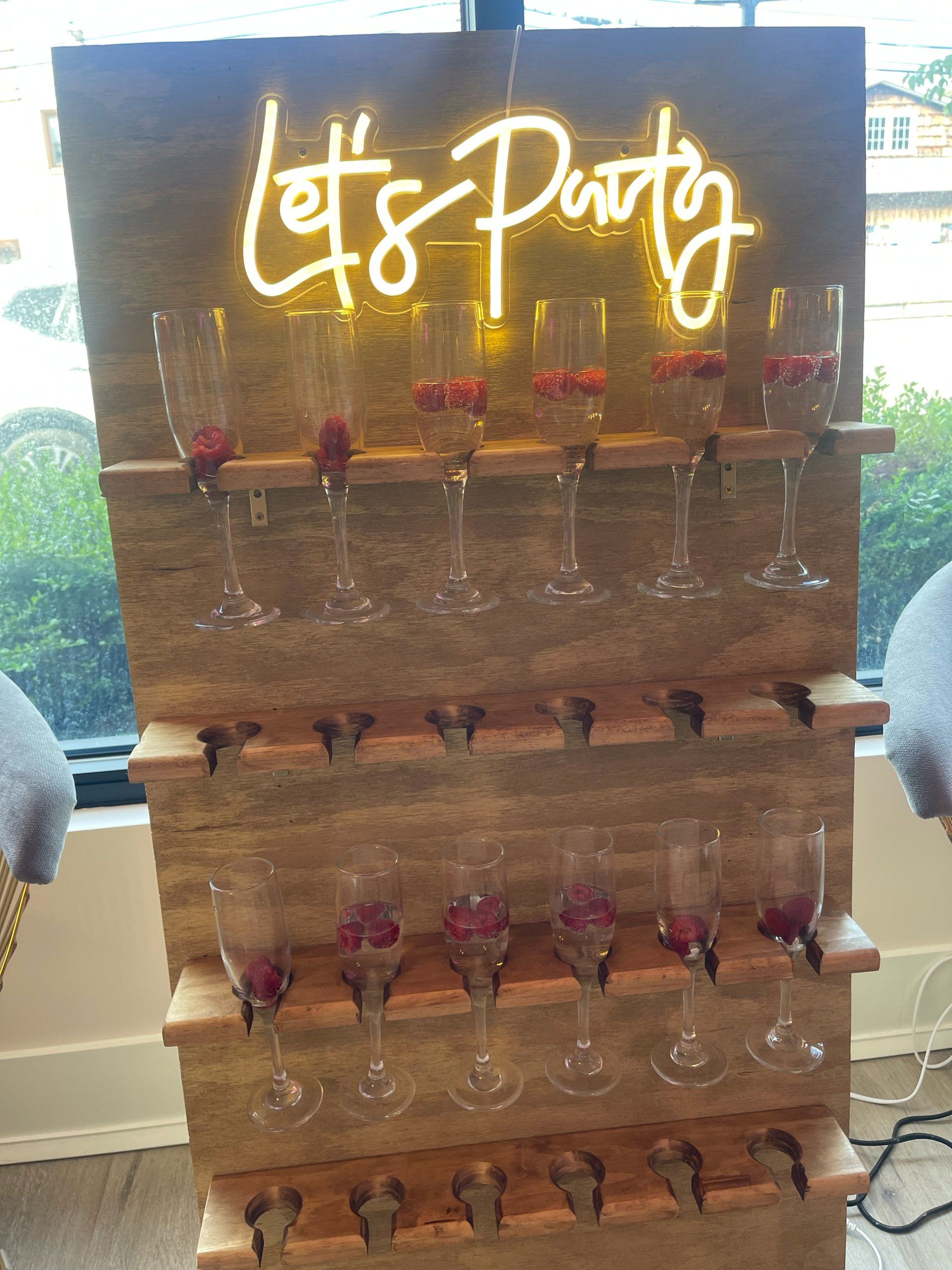 A wooden display with wine glasses and a neon sign that says `` let 's party ''.