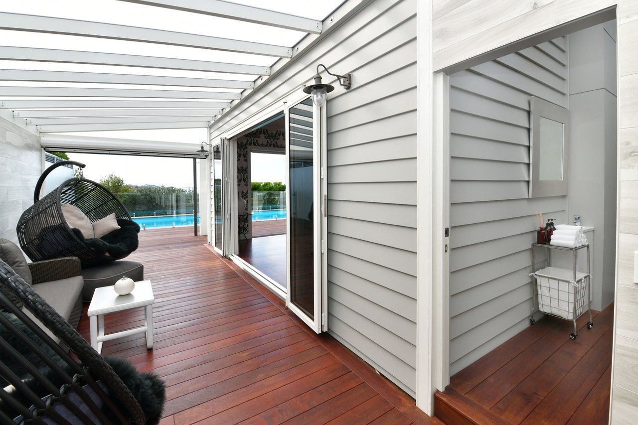 A white house with a wooden deck and a swimming pool in the background.