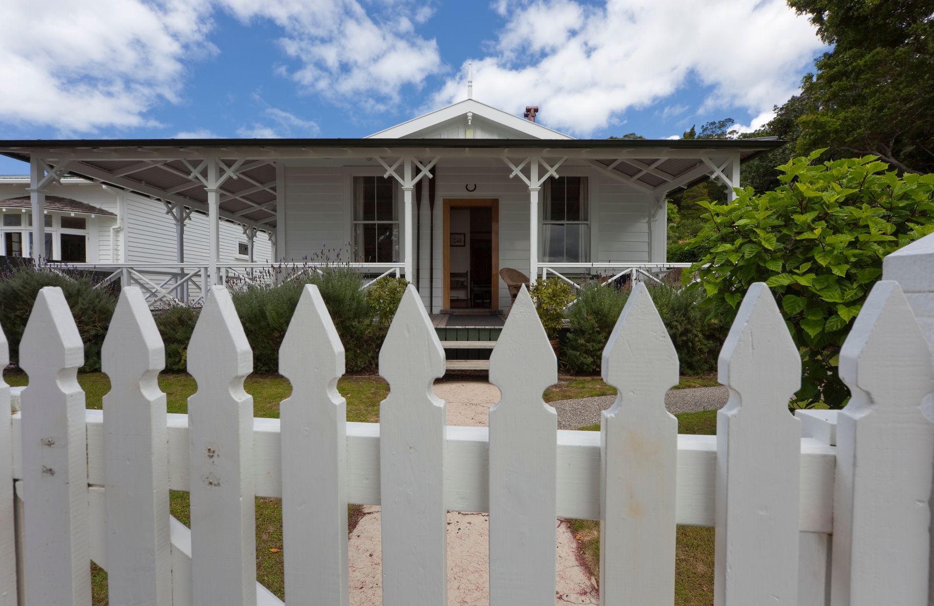 A white picket fence surrounds a white house with a porch.