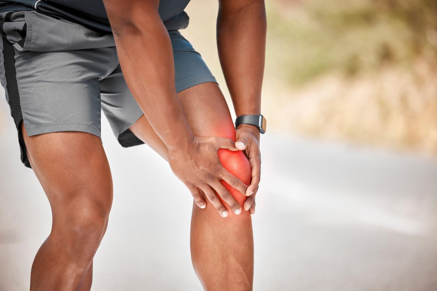 A person holding their knee, which is highlighted with a red glow to indicate pain or injury while outdoors.