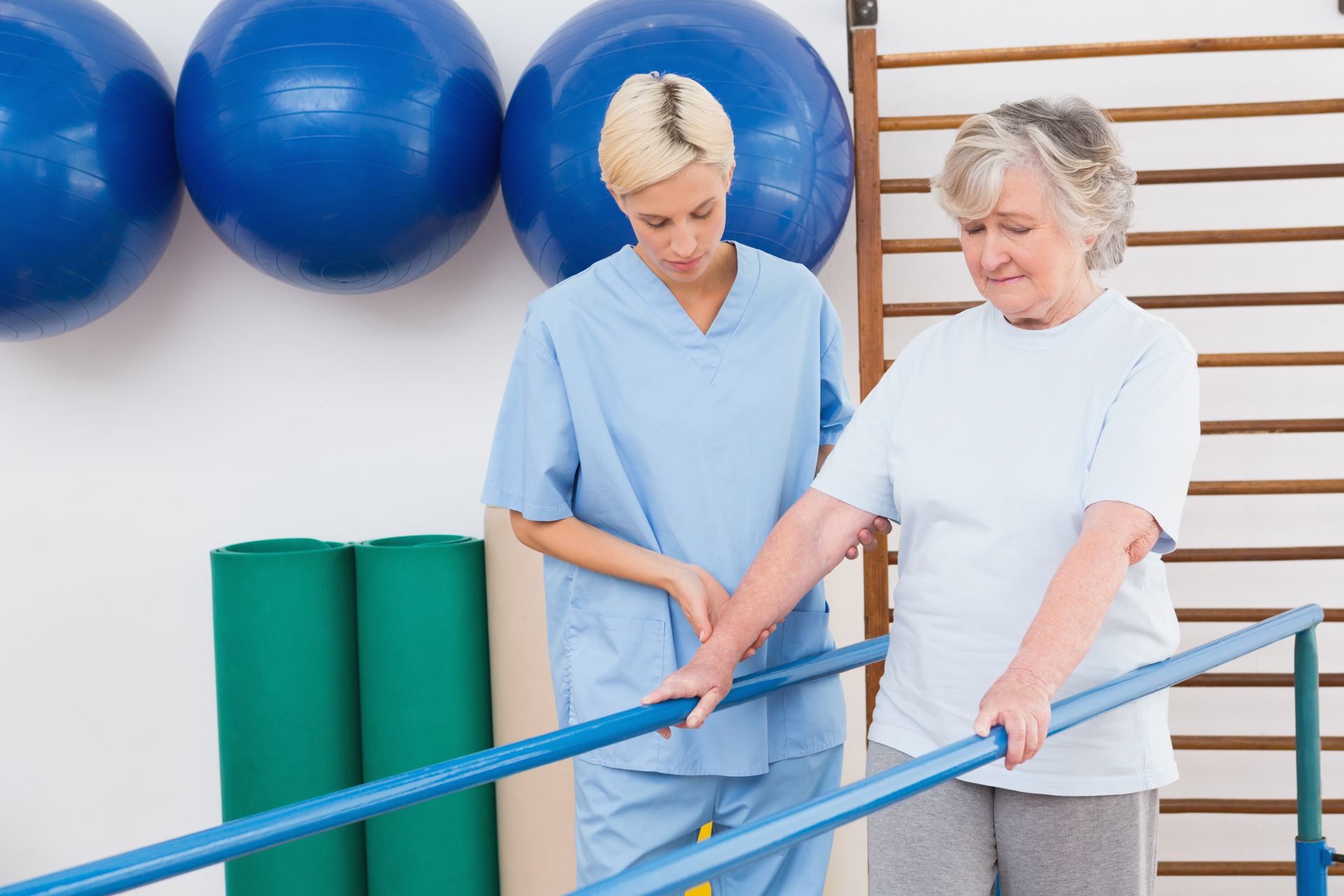 A nurse is helping an elderly woman walk on parallel bars.