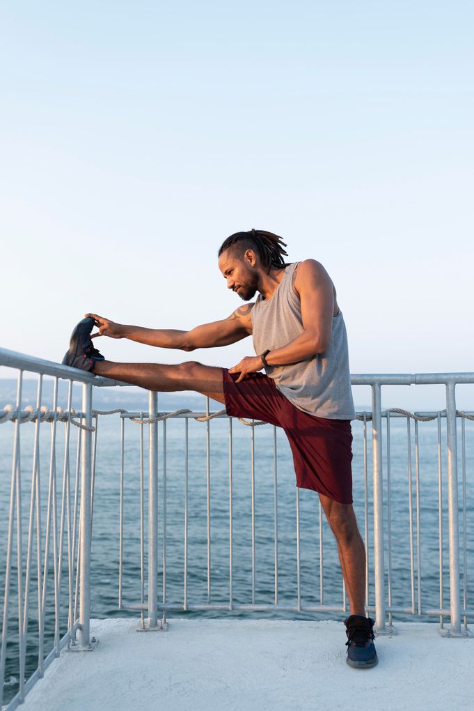a man stretches his leg on a railing overlooking the ocean