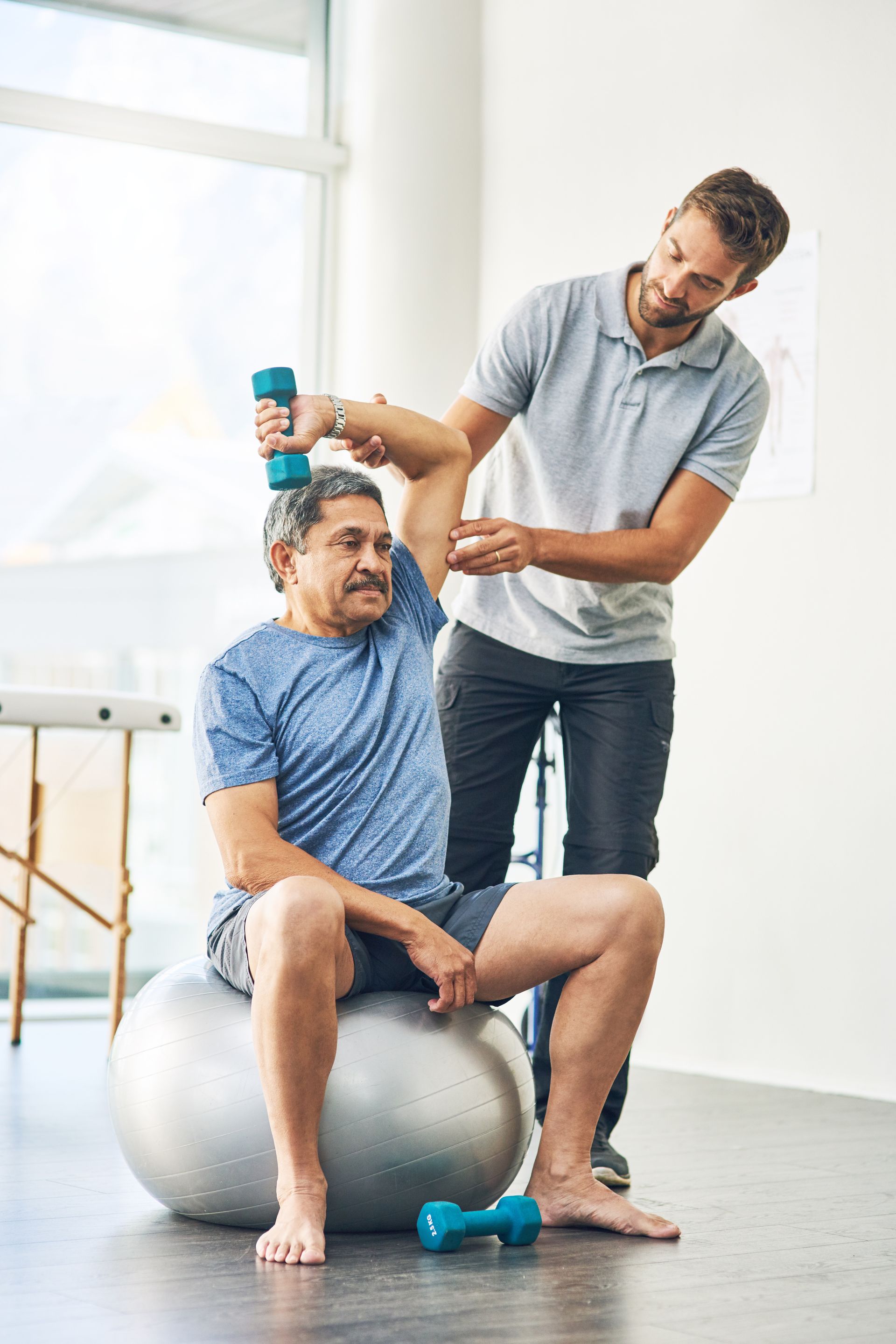 a man is sitting on an exercise ball while a man holds dumbbells