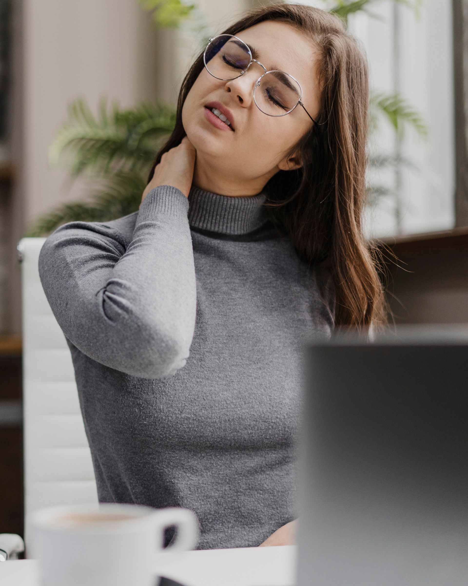 a woman wearing glasses holds her neck in pain
