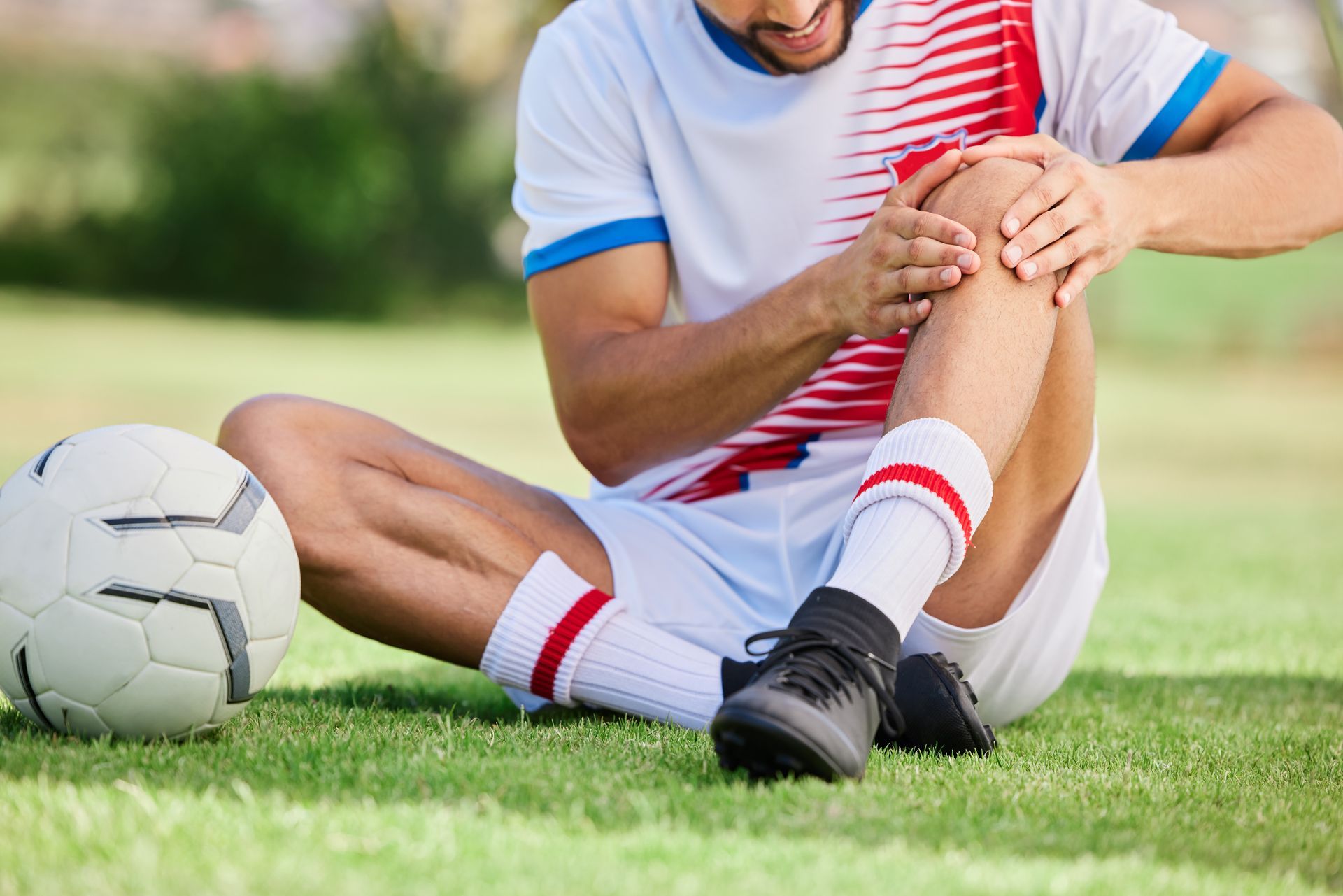 a soccer player is sitting on the grass with his knee in pain