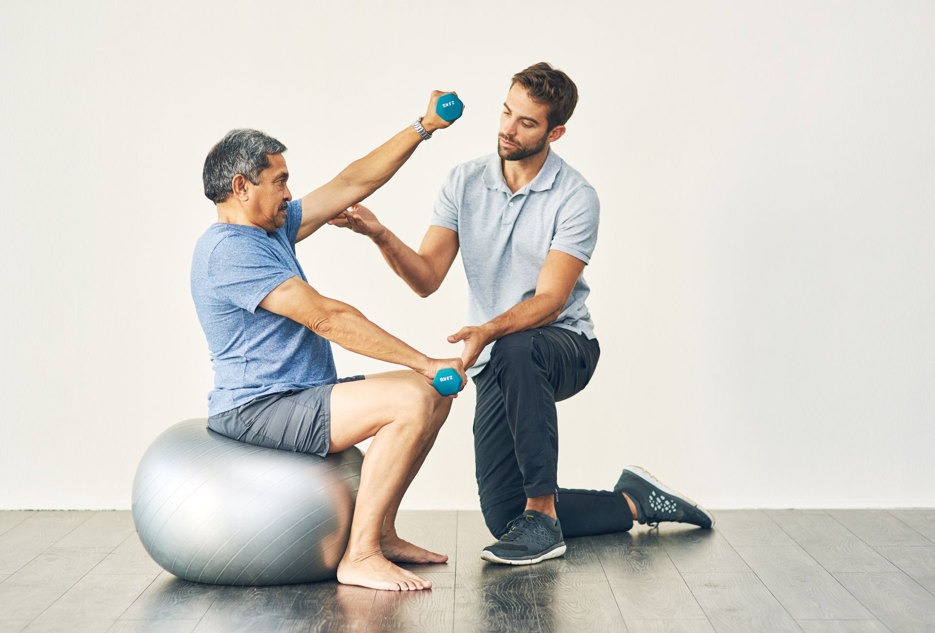 a man sits on an exercise ball while another man holds dumbbells