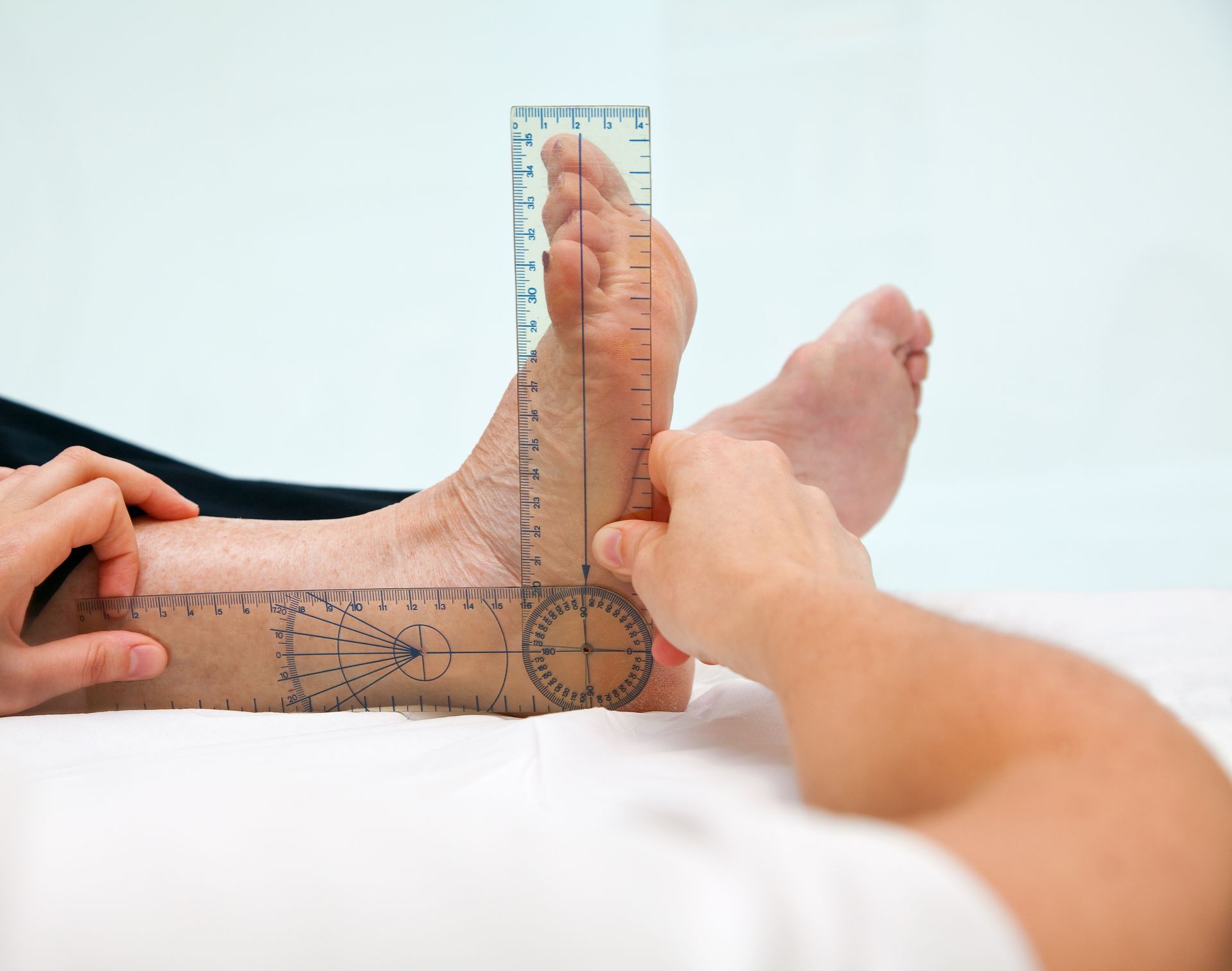 Person measuring a foot's angle with a ruler. Foot on a white surface, tattoos visible. Hands holding ruler.