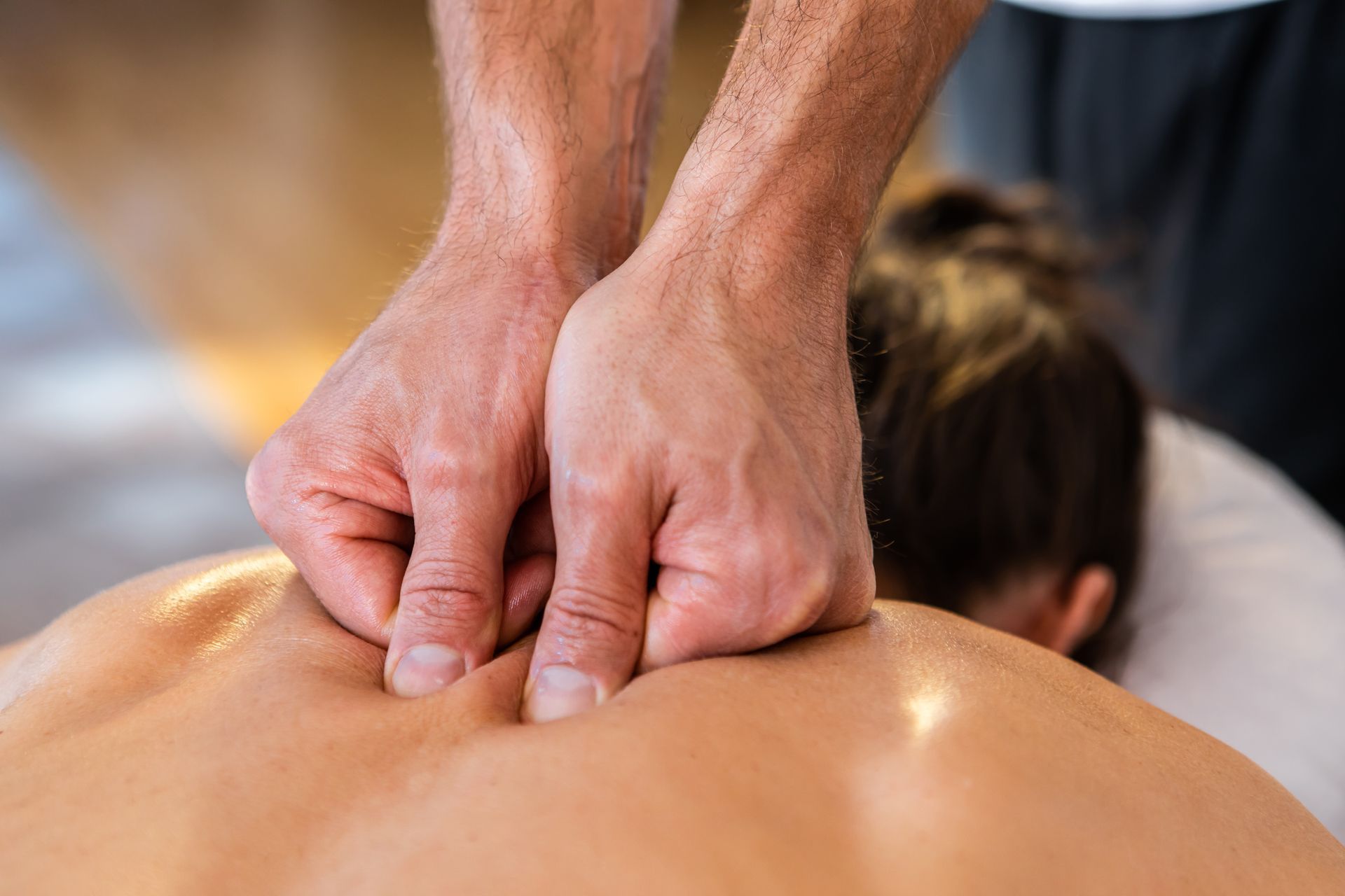 Hands massaging a person's upper back and shoulders.