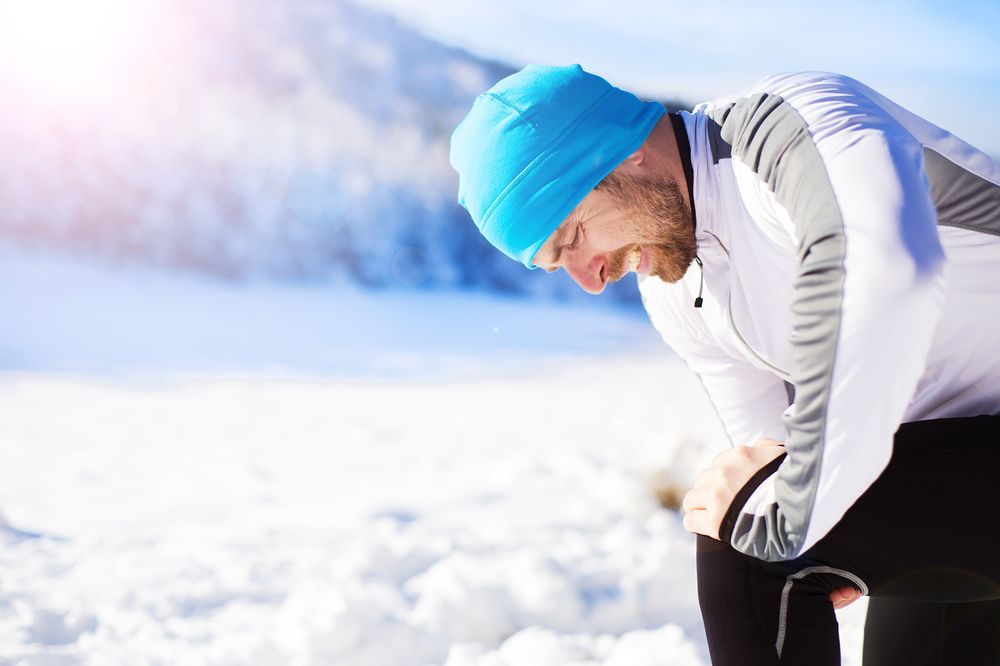 A man in a blue hat is kneeling down in the snow.