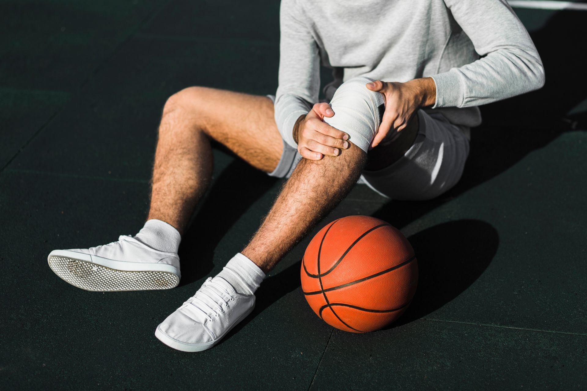 A man is sitting on the ground with a bandaged knee and a basketball.