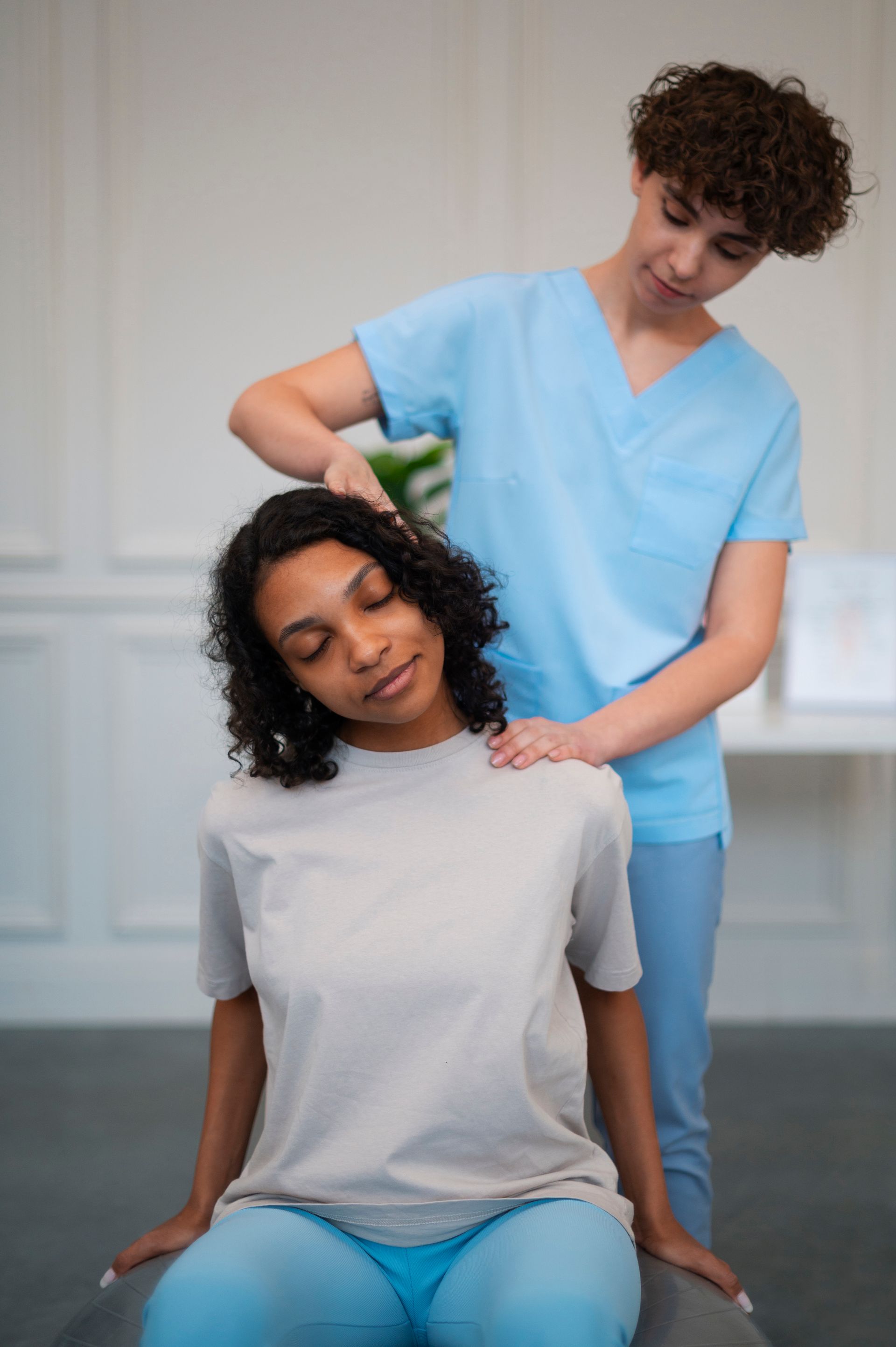 a woman in a white shirt is getting a massage from a woman in blue scrubs