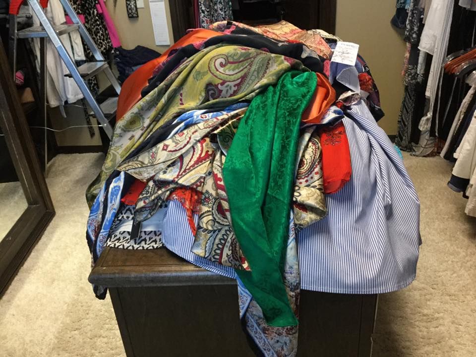Pile of colorful scarves and clothes atop a dark wooden chest in a closet.