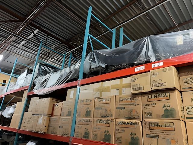 Warehouse shelving filled with U-Haul boxes and long items covered in black plastic.