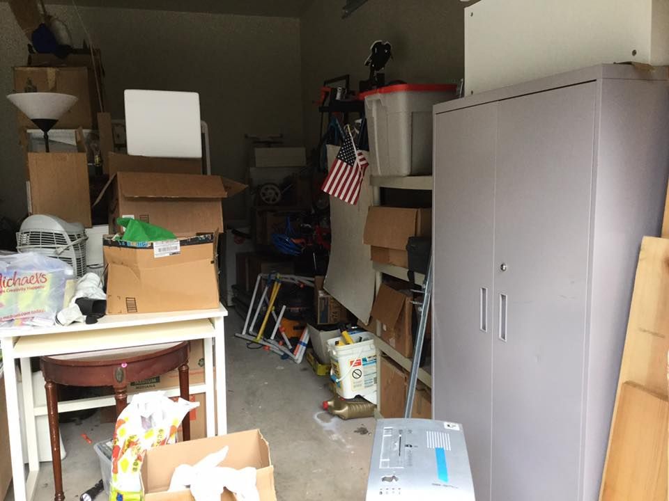 Cluttered garage with boxes, furniture, and storage cabinet; American flag visible.