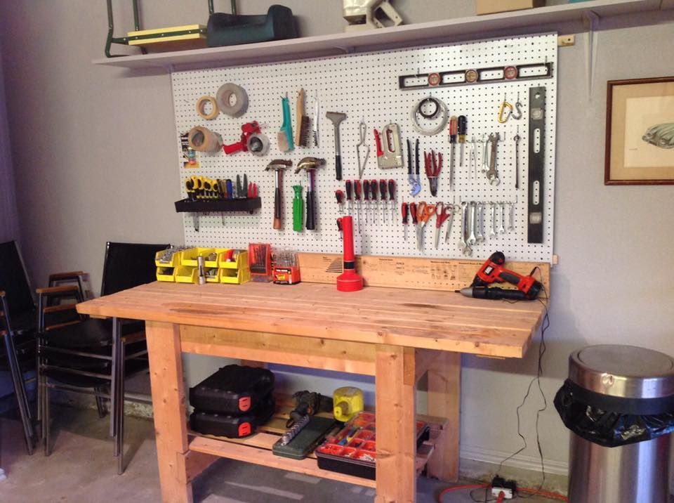 Workbench with tools on a pegboard, with tools and storage below, and a trash can nearby.