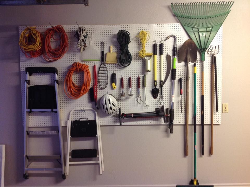Tools organized on a pegboard in a garage: ladders, rake, shovels, extension cords, and other hand tools.