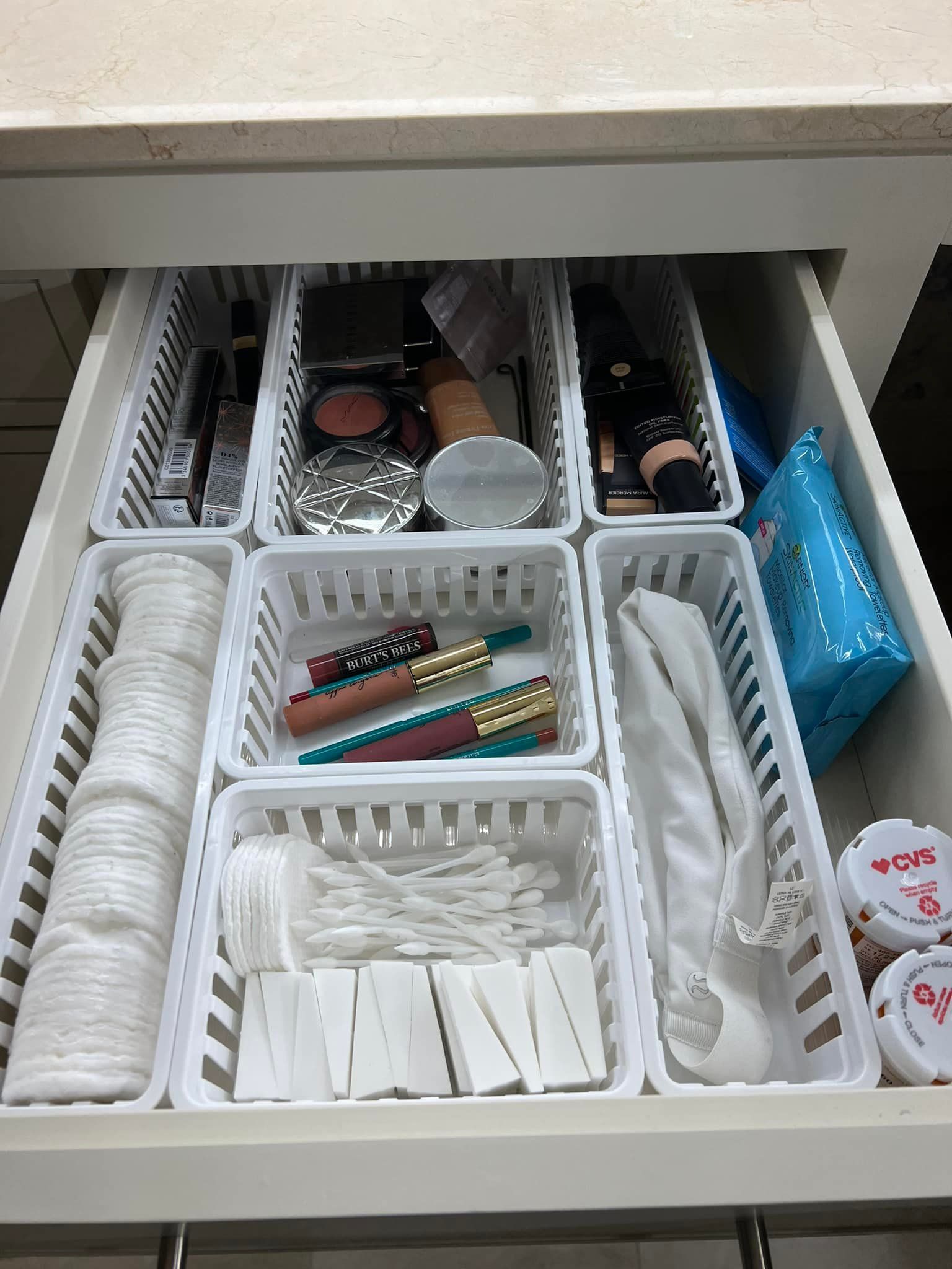 White drawer with organized makeup and supplies in white baskets.