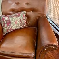 Brown leather armchair with a patterned pillow, near a window.