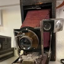 Close-up of an antique camera with a red bellows and a gold lens.
