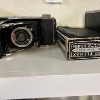 Black vintage camera and film box on a white shelf.